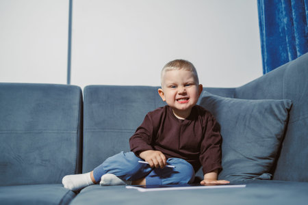 Young child is seated on a blue couch with a pencil in hand, focusing on a piece of paper on the...
