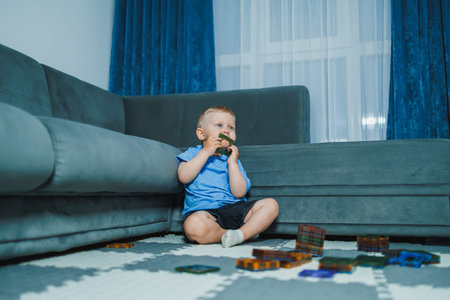 A young child plays on the floor of a living room. The child sits near a couch, holding a toy and...