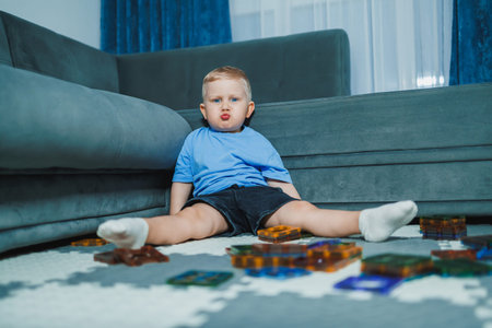 A child sits on the floor with toys spread around. The child looks focused while playing. Sunlight...