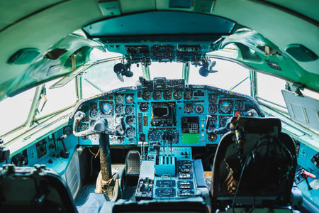 The cockpit of a large aircraft is filled with various control panels and instruments. Sunlight lights up the cockpit area. Two pilot seats are visible in the cabin.
