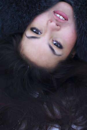 Face portrait of young attractive brunette woman lying on the snow. Perfect hair texture. Outdoor winter photo.の写真素材