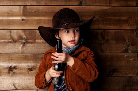 studio portrait of little cowboy with revolver behind wooden wallの写真素材