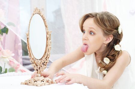 beautiful little girl with mirror showing her tongueの写真素材