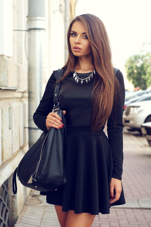 portrait of stylish beautiful girl wearing short black dress posing or walking at the streetの写真素材