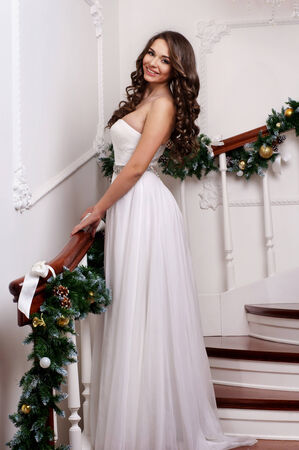 Young pretty woman wearing long white dress posing at christmas decorated stairwayの写真素材