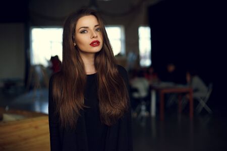 Natural light indoor portrait of young pretty girl with long dark brown hair, natural makeup and red lips. Stylish woman looking at youの写真素材