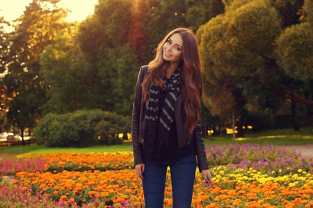 young beautiful stylish womanl posing against colorful flowers and trees at sunset. Fashion style autumn or fall portrait of pretty girl standing outdoorsの写真素材