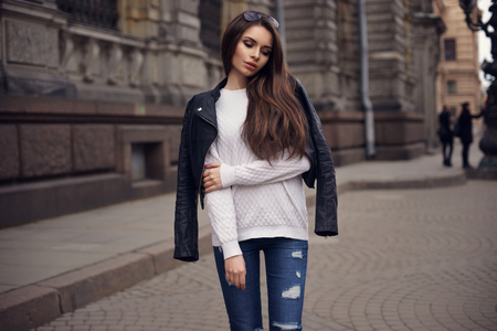 Fashion style portrait of young beautiful calm female model posing at city street with magnificent architecture. Full body portrait.の写真素材