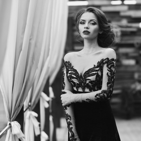 Young stunning beautiful pretty woman in black lace luxury evening dress posing at terracce. Fashion vogue style portrait in black and white colors