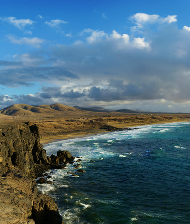 View on a coastline with huge rocks and sandy beach on a sunny evening with soft light. Mountains at...