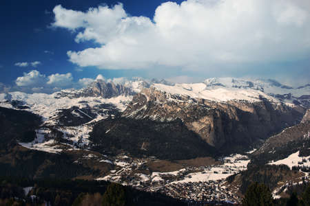 View on a village in alpine valley, snowy mountains and blue sky on a sunny spring dayの写真素材