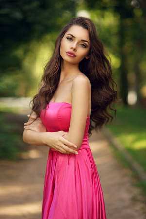 Pretty young model dressed in long evening dress posing outdoors at path in the park.の写真素材