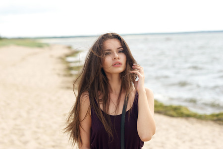 Portrait of young beautiful pretty girl with long brunette hair looking and camera and posing at beachの写真素材