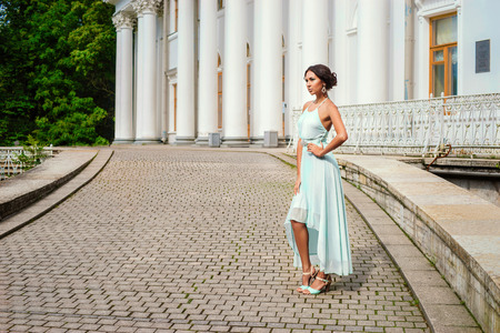 Full length portrait of young beautiful woman in light blue dress posing at pavment street against building with columnsの写真素材