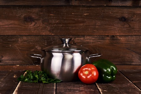 One stainless steel pot with glass cap standing on old grunge wooden table. Fresh vegetables. Tomato, parsley and green sweet pepperの写真素材