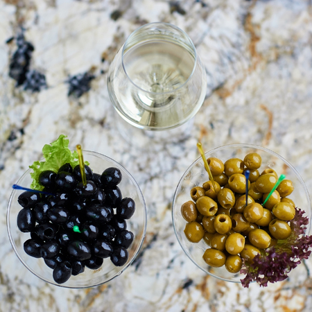 Appetizer. Green and black olives served in martini glasses with glass of white wine on marble table. Top view or flat lay.の写真素材