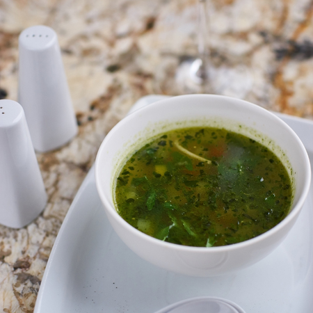 Minestrone soup with arugula served in a white bowl with ceramic spoon, glass of white wine on marble tableの写真素材