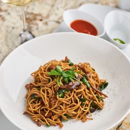 Flat egg noodles with duck meat, chicken, shiitake mushrooms served on white plate with white garlic and red spicy sauceの写真素材