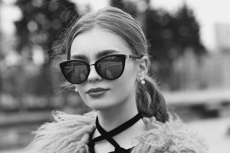 Stylish red hair girl with ponytail wearing short black dress, fur coat and sunglasses. Young woman with pink tulipsの写真素材