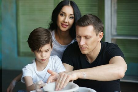 Young caucasian family working on potters wheel. Handsome father, beautiful mother and young son. Pottery classes. Dirty Hands. Parents enjoying time together with their child.の写真素材