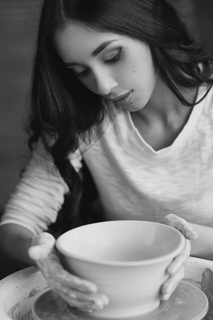 Young beautiful pretty woman with brunette dark hair working on pottery wheel and sculpting clay potの写真素材
