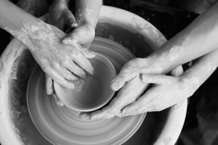 Family working on pottery wheel. Top view of mother, father and son hands making ceramic pot or sculpting clayの写真素材