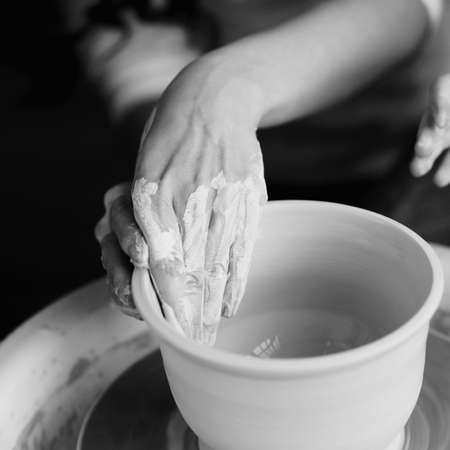 Woman working on potters wheel making dishes with their own hands. Close-up photo of dirty hands molding clay.の写真素材