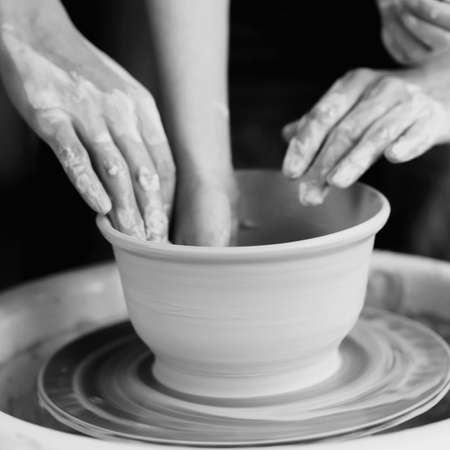 Mother teaches son to work on pottery wheel. Close up of dirty hands sculpting clay.の写真素材