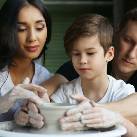 Family working on pottery wheel. Mother and father teaching their son to scupl or make clay potの写真素材