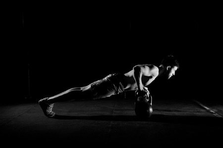 Fitness training. Man doing push ups exercise using dumbbells or weights in dark gym.の写真素材