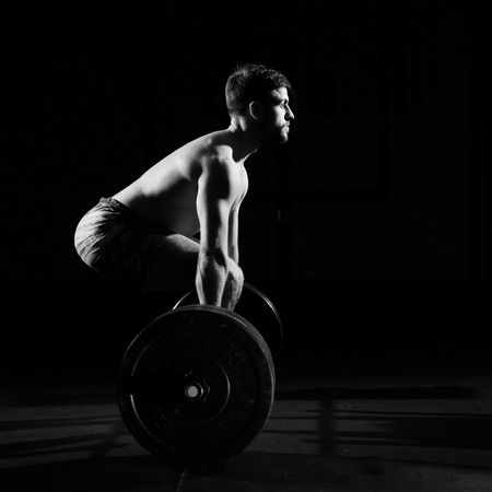 Fitness training. Man doing exercises or training with barbell in dark gym.の写真素材