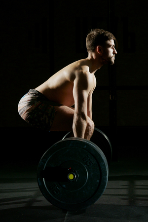 Fitness training. Man doing exercises or training with barbell in dark gym.の写真素材