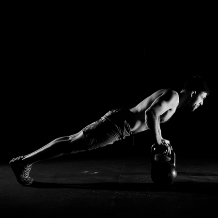 Fitness training. Man doing push ups exercise using dumbbells or weights in dark gym.の写真素材