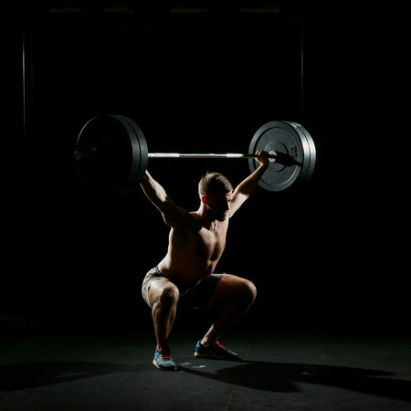 Fitness training. Man doing sit ups exercise with barbell in dark gym.の写真素材