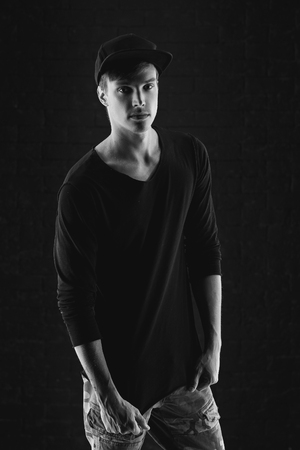 Fashion vogue style portrait of young handsome man in black pullover and cap posing against brick wall background.の写真素材