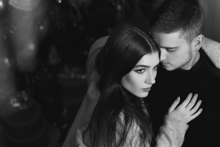 Closeup portrait of young romantic caucasioan couple sitting and higging in christmas decorated interior. Cute lovers staying at home and enjoying tome togetherの写真素材