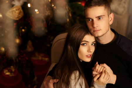 Closeup portrait of young romantic caucasioan couple sitting and higging in christmas decorated interior. Cute lovers staying at home and enjoying tome togetherの写真素材