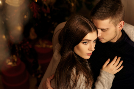 Closeup portrait of young romantic caucasioan couple sitting and higging in christmas decorated interior. Cute lovers staying at home and enjoying tome togetherの写真素材