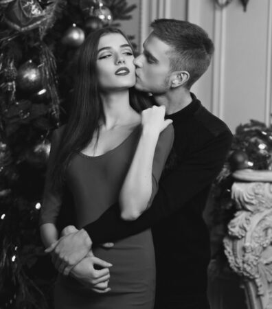 Young romantic couple standing and hugging in christmas decorated home interior. Pretty woman in red dress and man in blackの写真素材