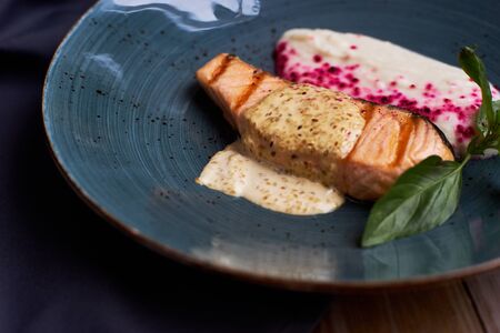Grilled salmon steak with cauliflower cream and sesame creamy sauce on blue ceramic plate on wooden tableの写真素材
