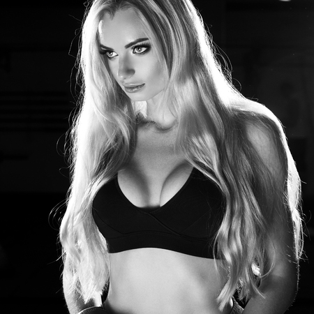 Half portrait of young blonde woman with long hair, dressed in black sports bra, pink shorts and red boxing gloves, looking to right side. Lovely female boxer posing. Concept of strength and power.の写真素材