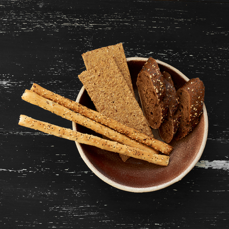 Different bread slices in brown ceramic bowl standing on blue wooden aged surface. Top view.