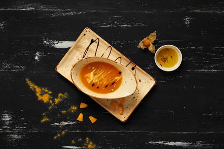 Tasty creamy pumpkin soup in oval bowl and rectangular plate standing on blue aged wooden table. Appetizing restaurant vegan meal served with bread slices, delicious veggie recipe. Top view.の写真素材