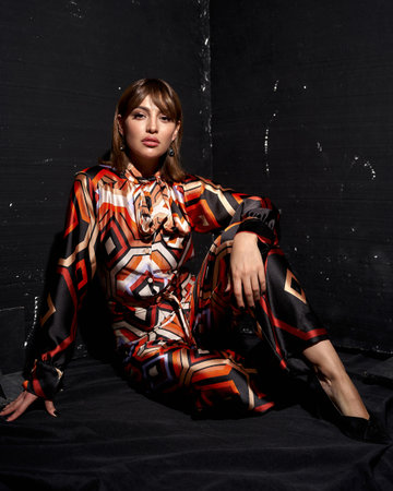 A stylish woman poses in a vibrant geometric print outfit with bold red, orange, and black tones, exuding fashion-forward elegance.の写真素材