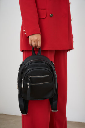 Stylish blonde woman poses with a trendy black backpack in a fashion studio setting