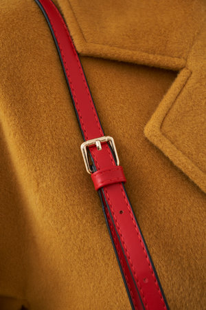 Camel-colored wool coat features a striking red leather strap with a silver buckle. The close-up...