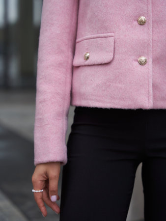 A person wearing a pink jacket with gold buttons and black pants. The hand, adorned with rings, rests casually by the side. The jacket features a flap pocket with a buttonの写真素材