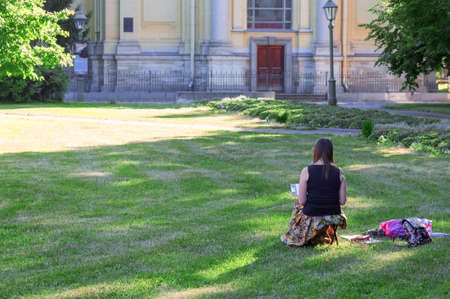A young girl artist paints in the park sitting with her backの写真素材