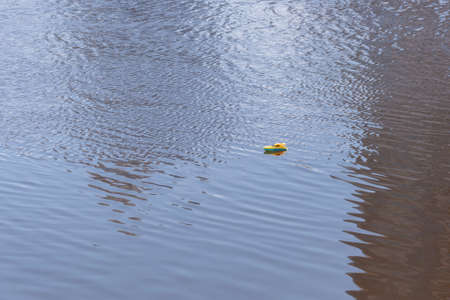 A small yellow lonely boat is floating in the water. A toyの写真素材