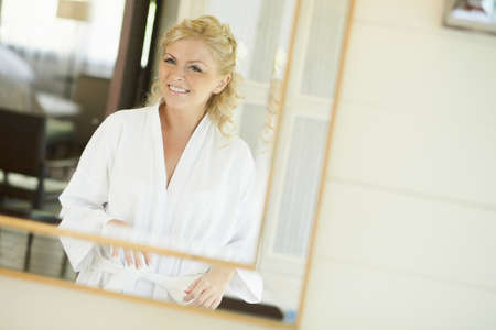 Gorgerous bride standing in front of mirror and fixing her hair and make up. Putting earings, powdering and smilling.の写真素材